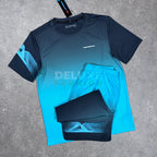 A two-piece athletic set laid flat on a gray concrete surface, featuring a short-sleeve gradient shirt and matching shorts. The shirt has a dark navy-to-turquoise gradient with a geometric pattern on the sleeve, and the shorts are dark navy with a matching geometric pattern.